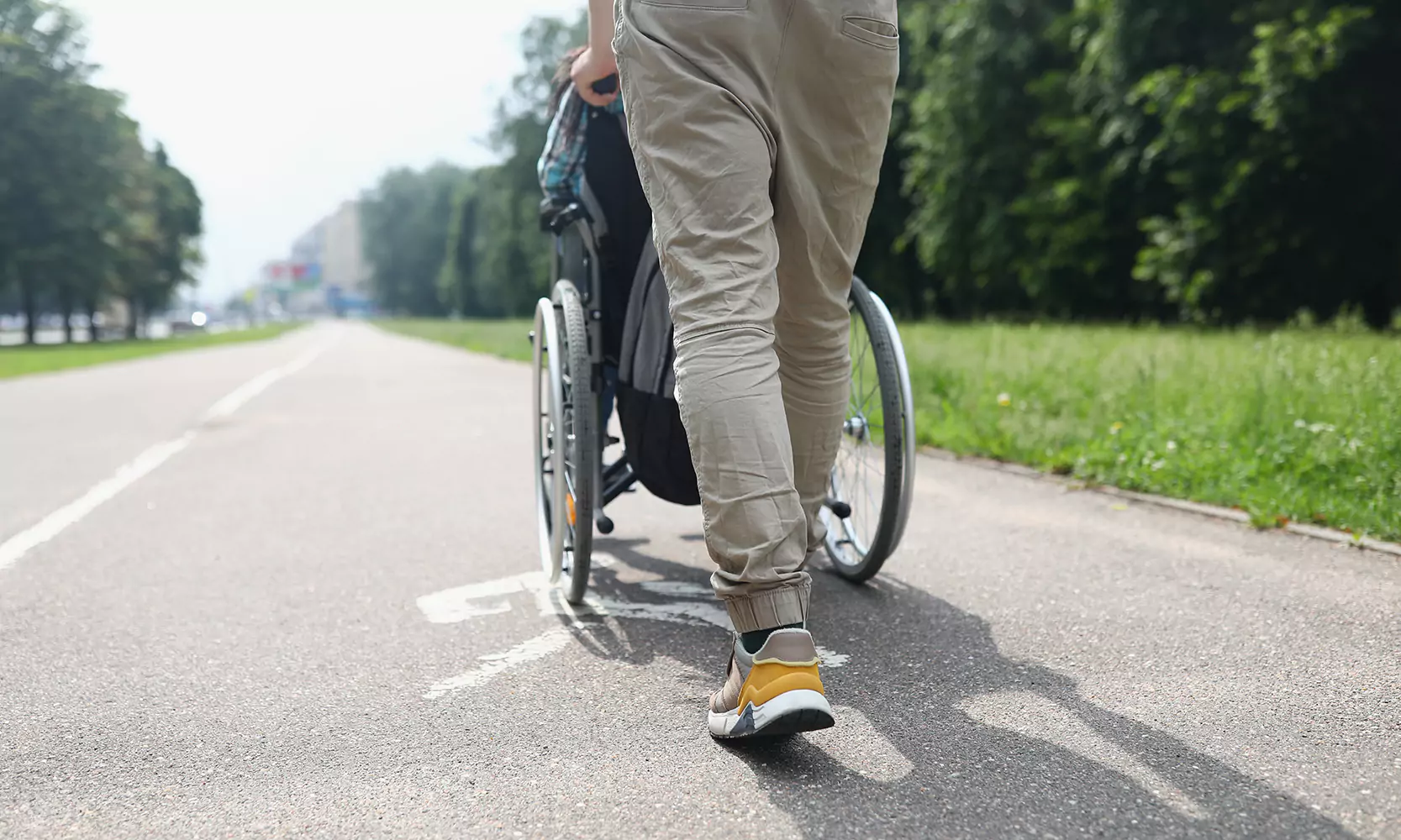 A caregiver pushing a wheelchair of a participant through a park