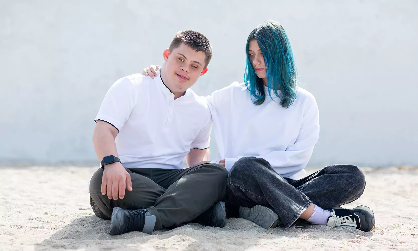 A boy with down syndrome and his sister sitting cross legged facing the camera