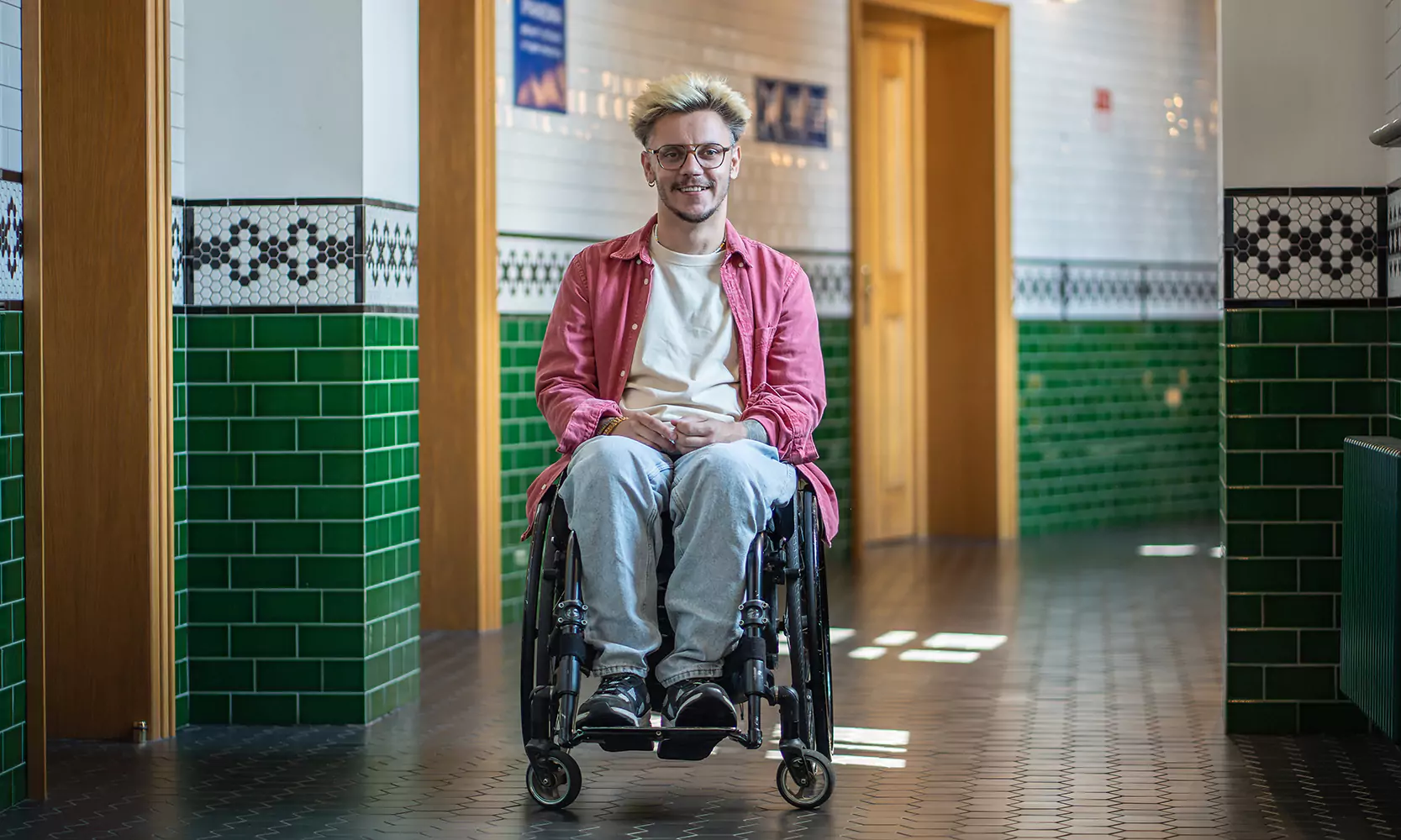 A young man with a physical disability is in his wheelchair smiling at the camera